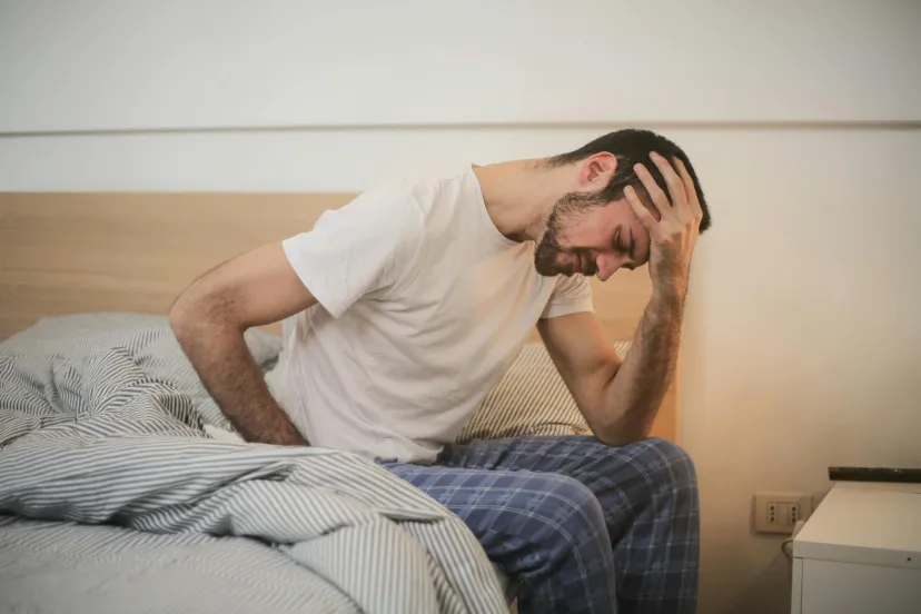 A man sitting on the edge of a bed with his head in his hand