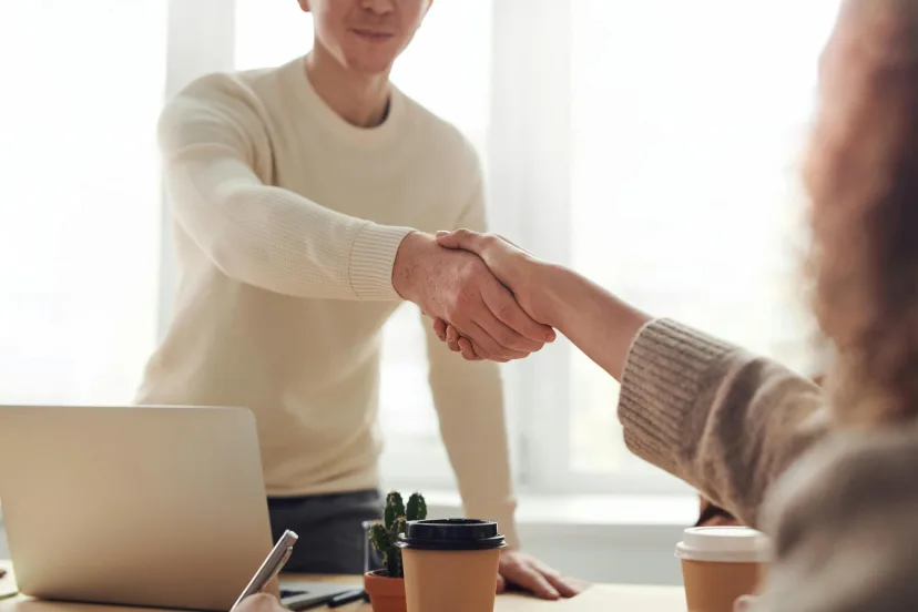 Two people shaking hands across a desk after an interview